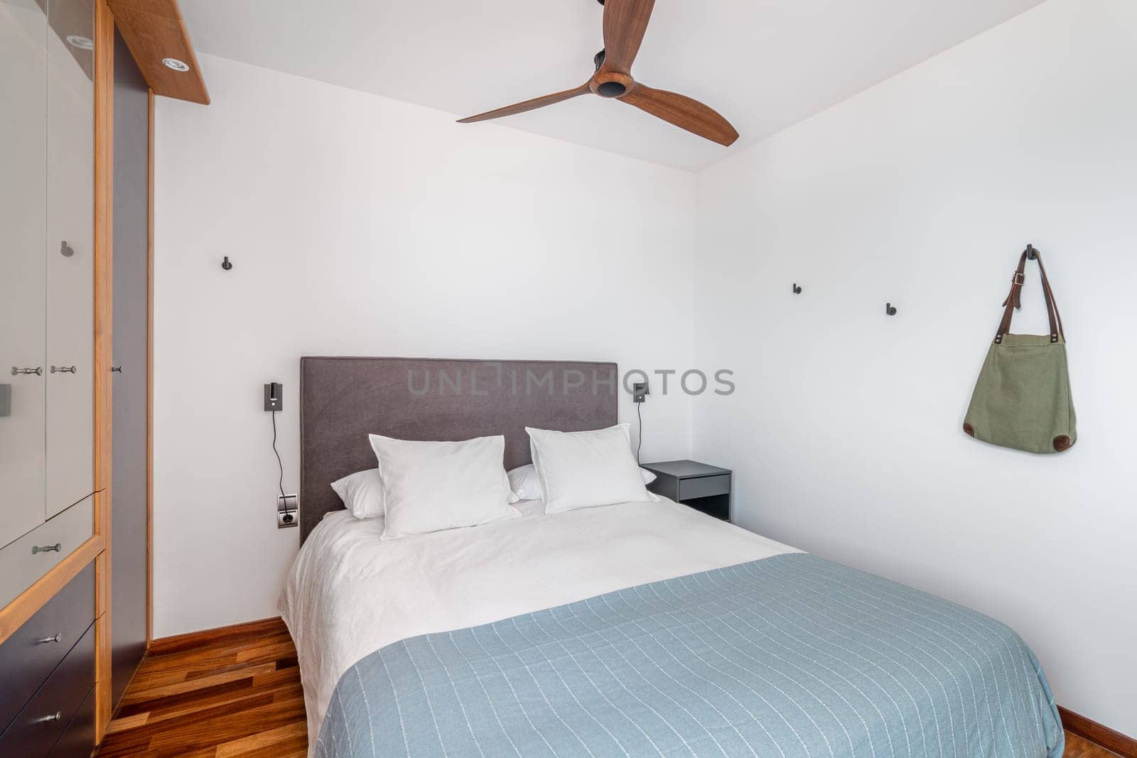 Soft place to sleep in contemporary hotel room. Large bed with pillows and blanket and fan on ceiling in renovated apartment. Interior design