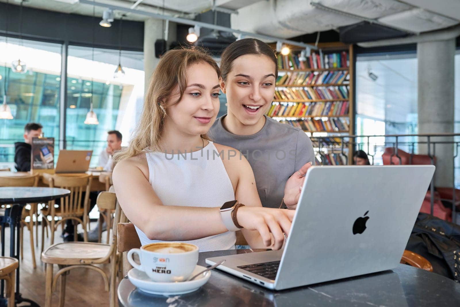 Warsaw, Poland, 12.05.2023. Two young teenage females in cafe using laptop, talking by VH-studio