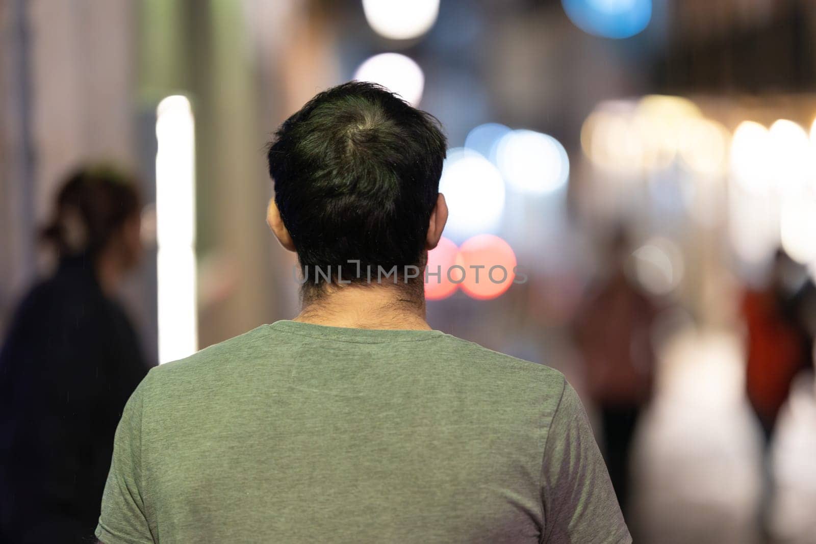 A man is seen walking alone, surrounded by the vibrant night lights of the city.