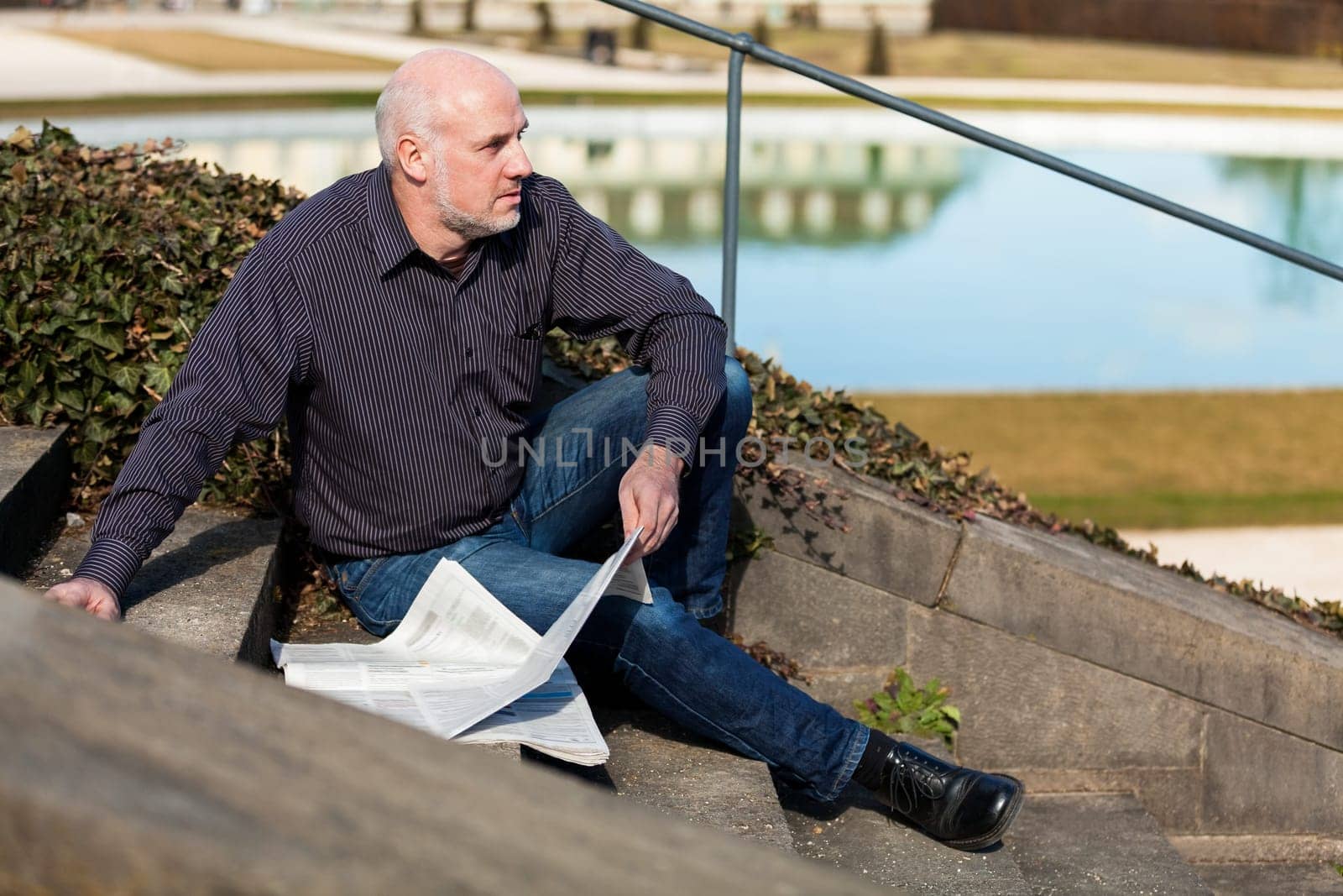 Middle-aged man,senior sitting with a newspaper on a staircase in spring outdoors