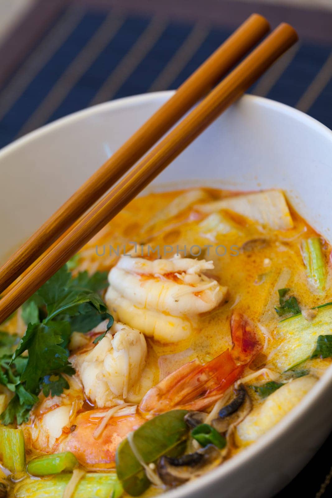 Bowl plate with freshly prepared Tom Yam soup with clanguste and coriander with chopsticks as close-up