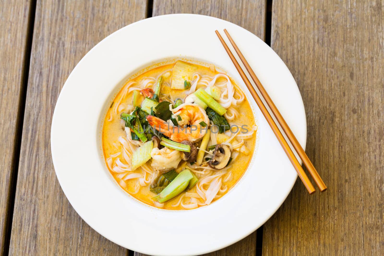 Bowl plate with freshly prepared Tom Yam soup with clanguste and coriander with chopsticks as close-up