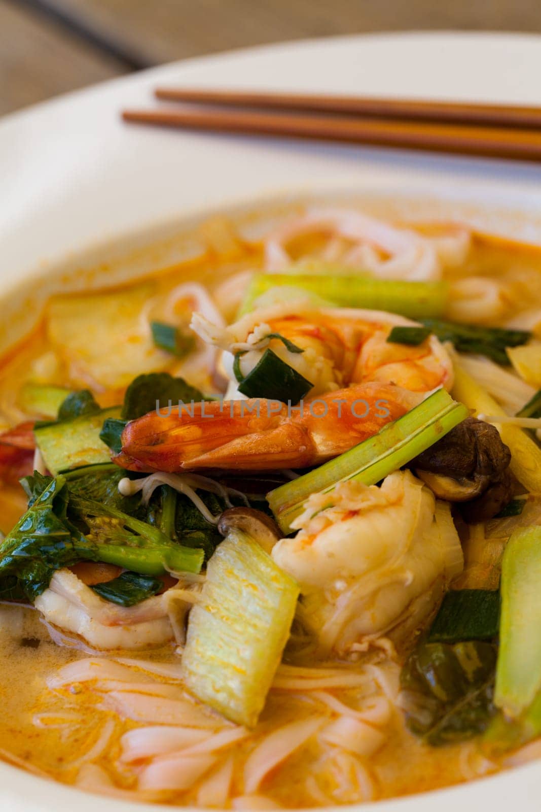 Bowl plate with freshly prepared Tom Yam soup with clanguste and coriander with chopsticks as close-up