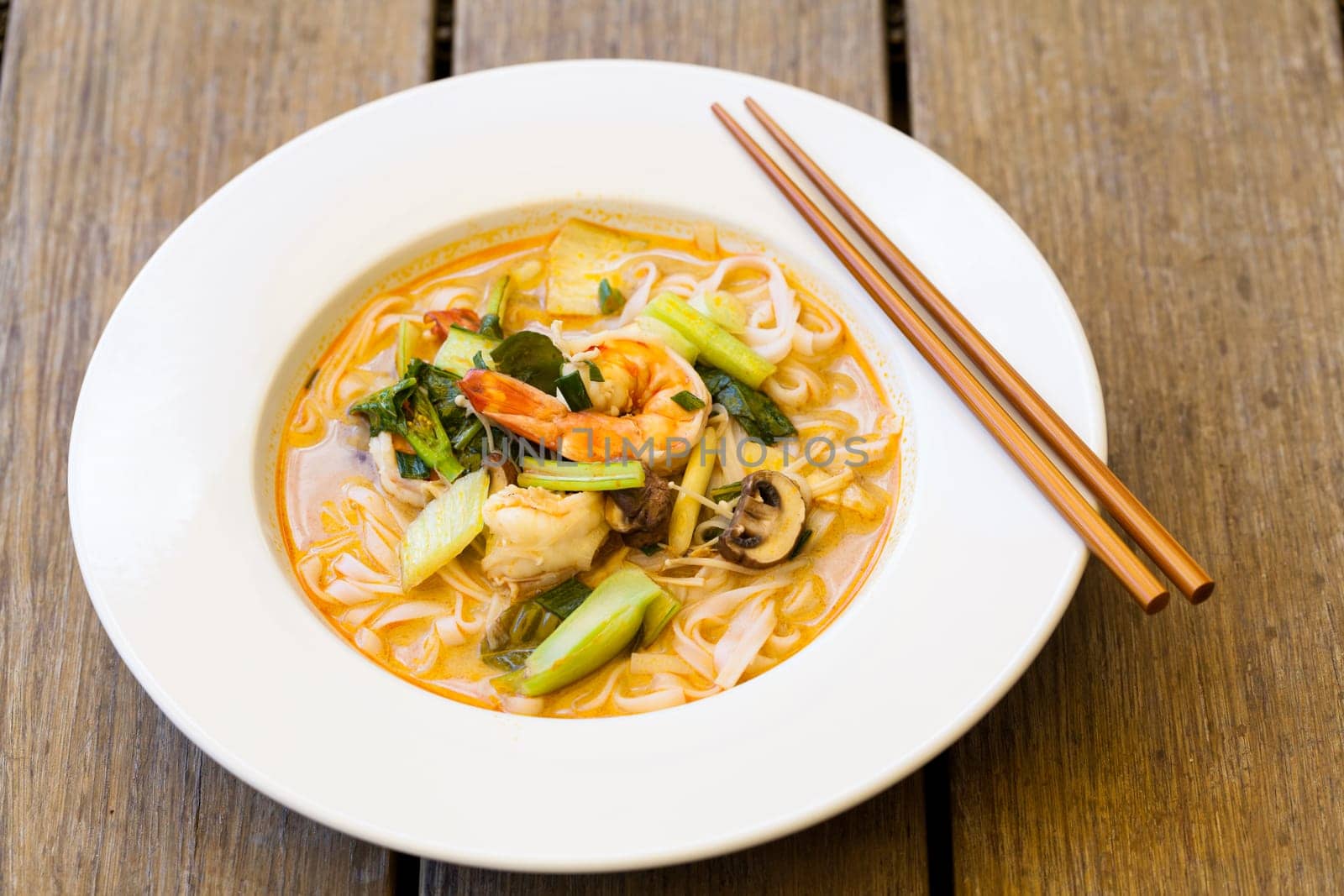 Bowl plate with freshly prepared Tom Yam soup with clanguste and coriander with chopsticks as close-up