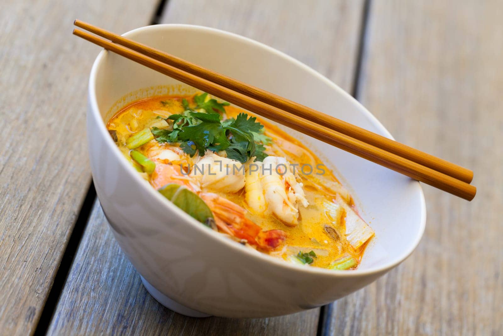 Bowl plate with freshly prepared Tom Yam soup with clanguste and coriander with chopsticks as close-up