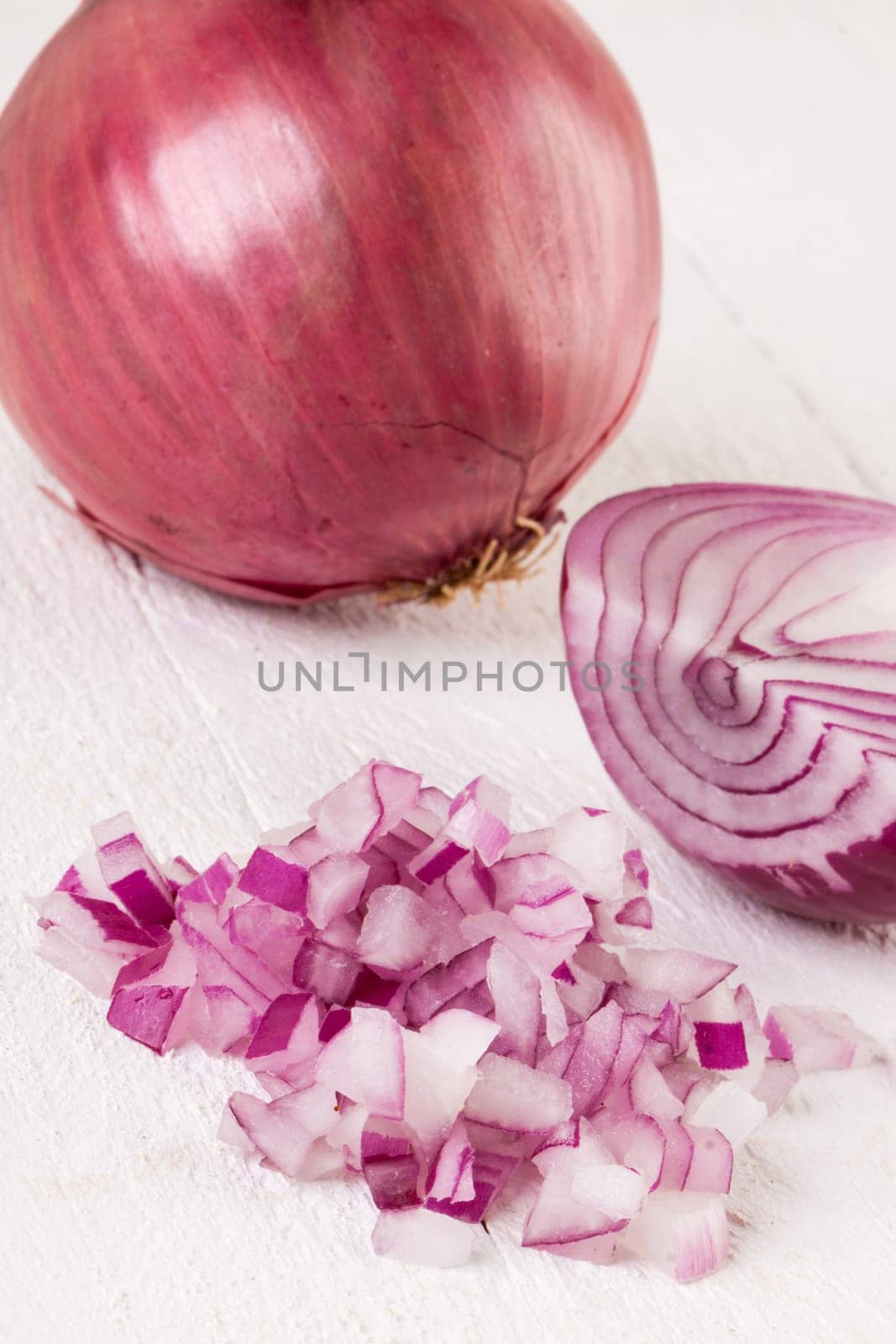 Red food onion whole and in small cubes Brunoise in a bowl on a white wooden board