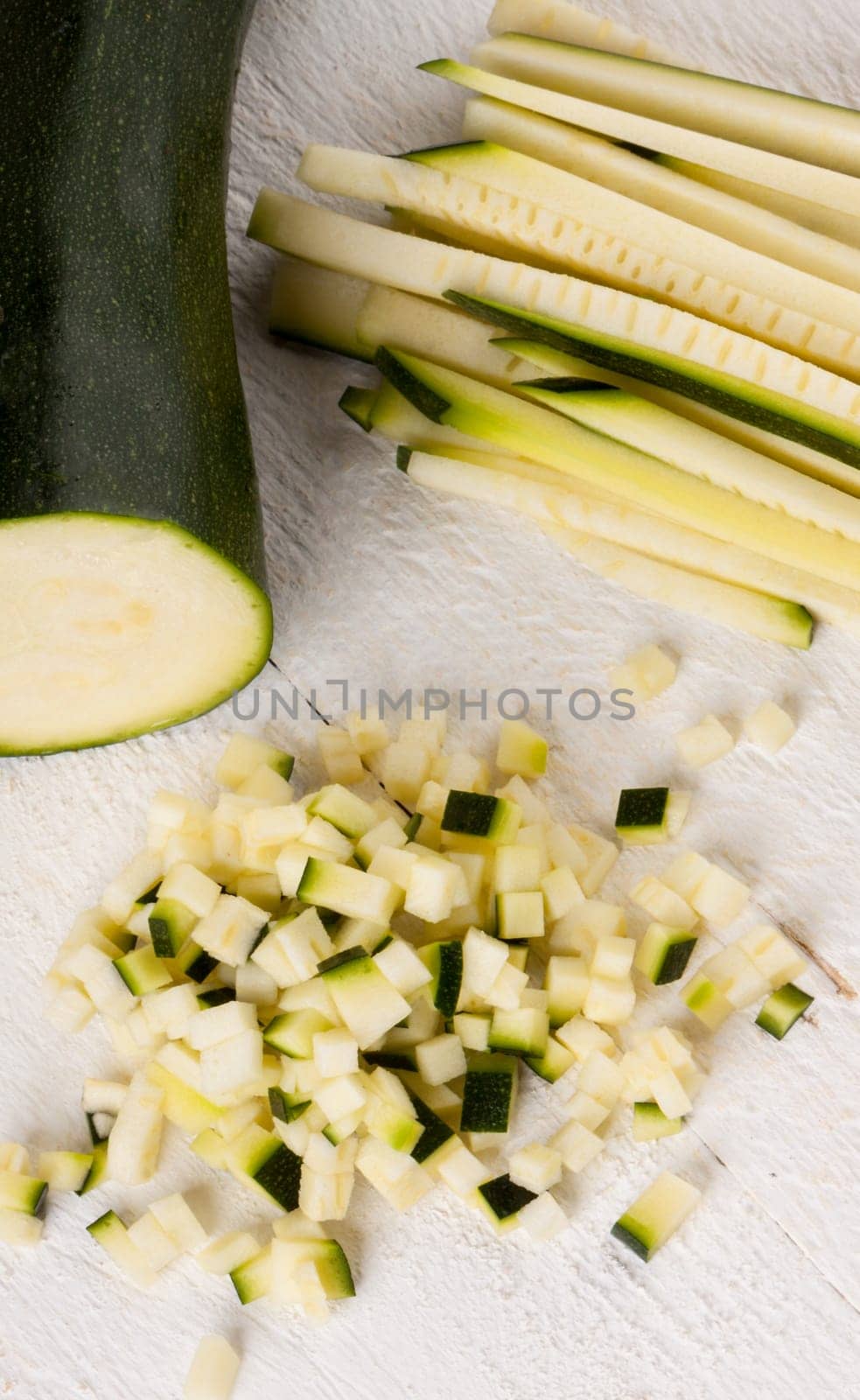 Fresh zucchini all in julienne strips and cut into brunoise cubes on a white hoözboard
