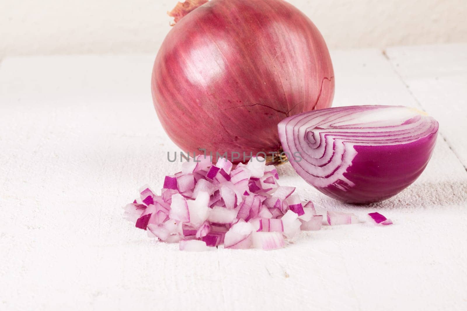 Red food onion whole and in small cubes Brunoise in a bowl on a white wooden board