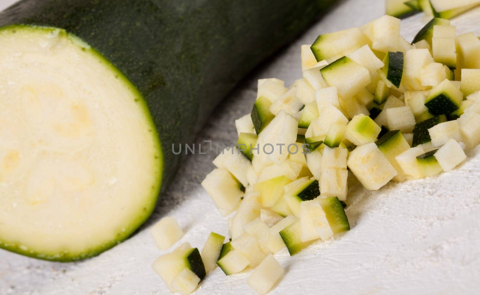 Fresh zucchini all in julienne strips and cut into brunoise cubes on a white hoözboard