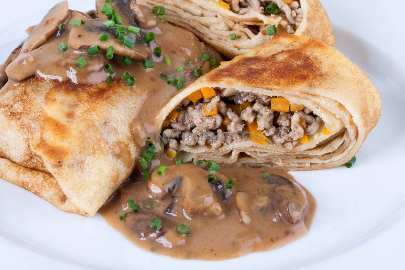 Pancake crepes tortillas stuffed with mushrooms and minced meat on a white plate close-up