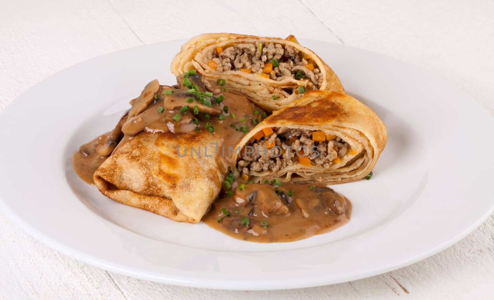 Pancake crepes tortillas stuffed with mushrooms and minced meat on a white plate close-up