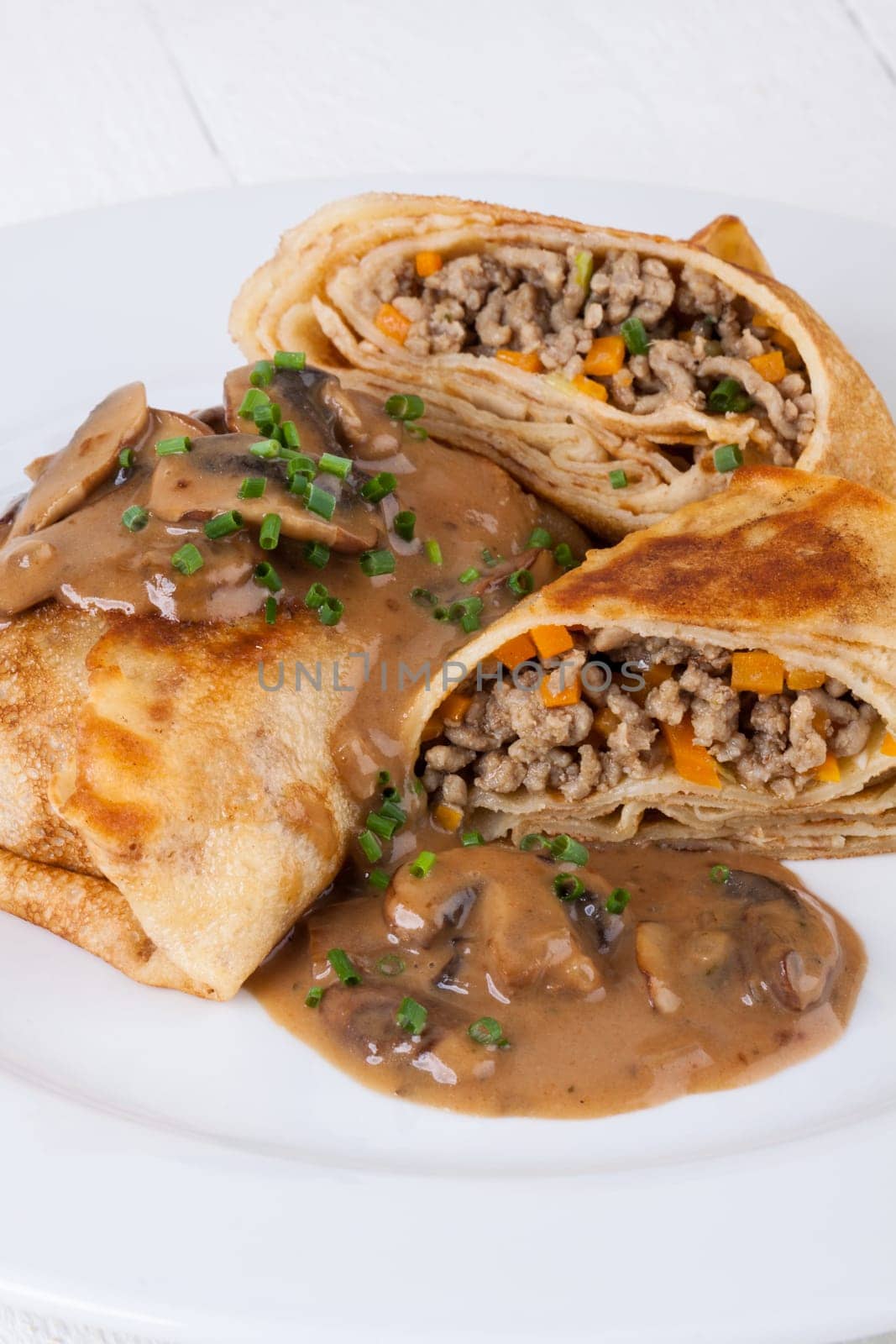 Pancake crepes tortillas stuffed with mushrooms and minced meat on a white plate close-up