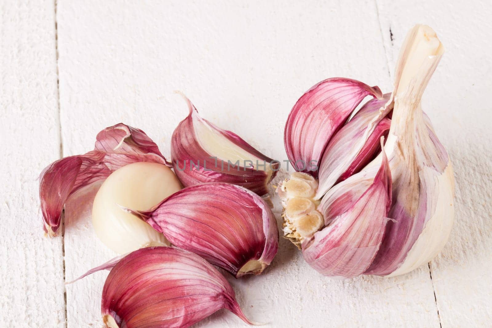 Garlic tuber with toes Fresh in whole and as a detail as a close-up on white wood