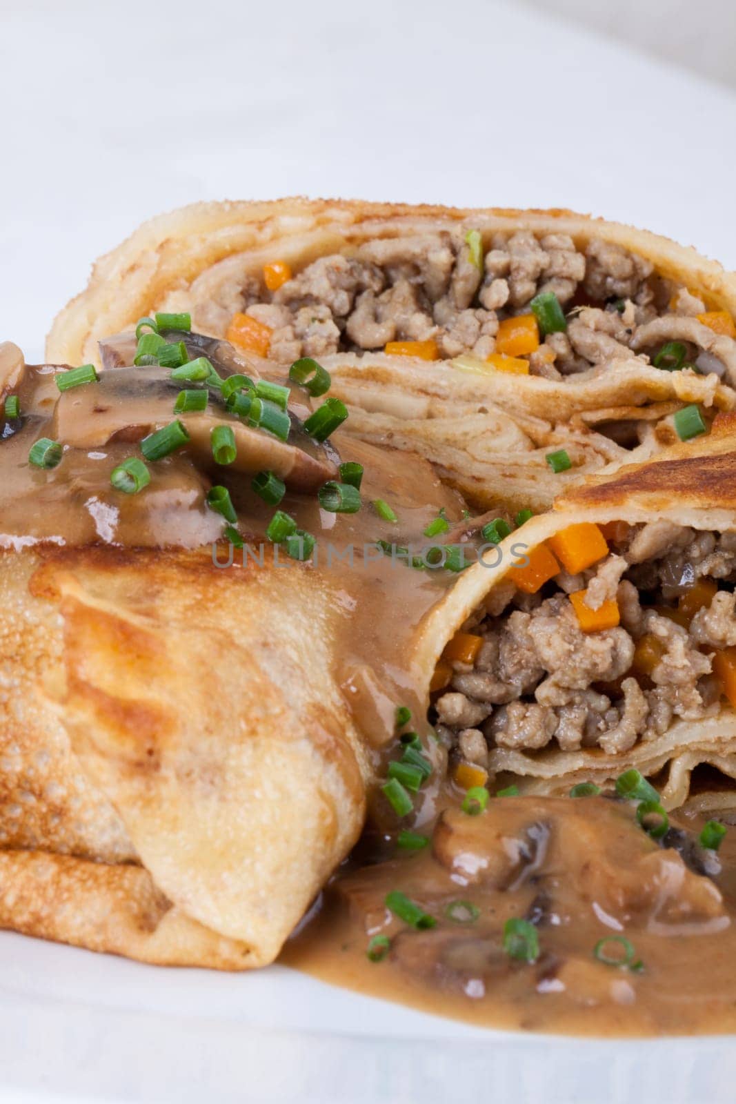 Pancake crepes tortillas stuffed with mushrooms and minced meat on a white plate close-up