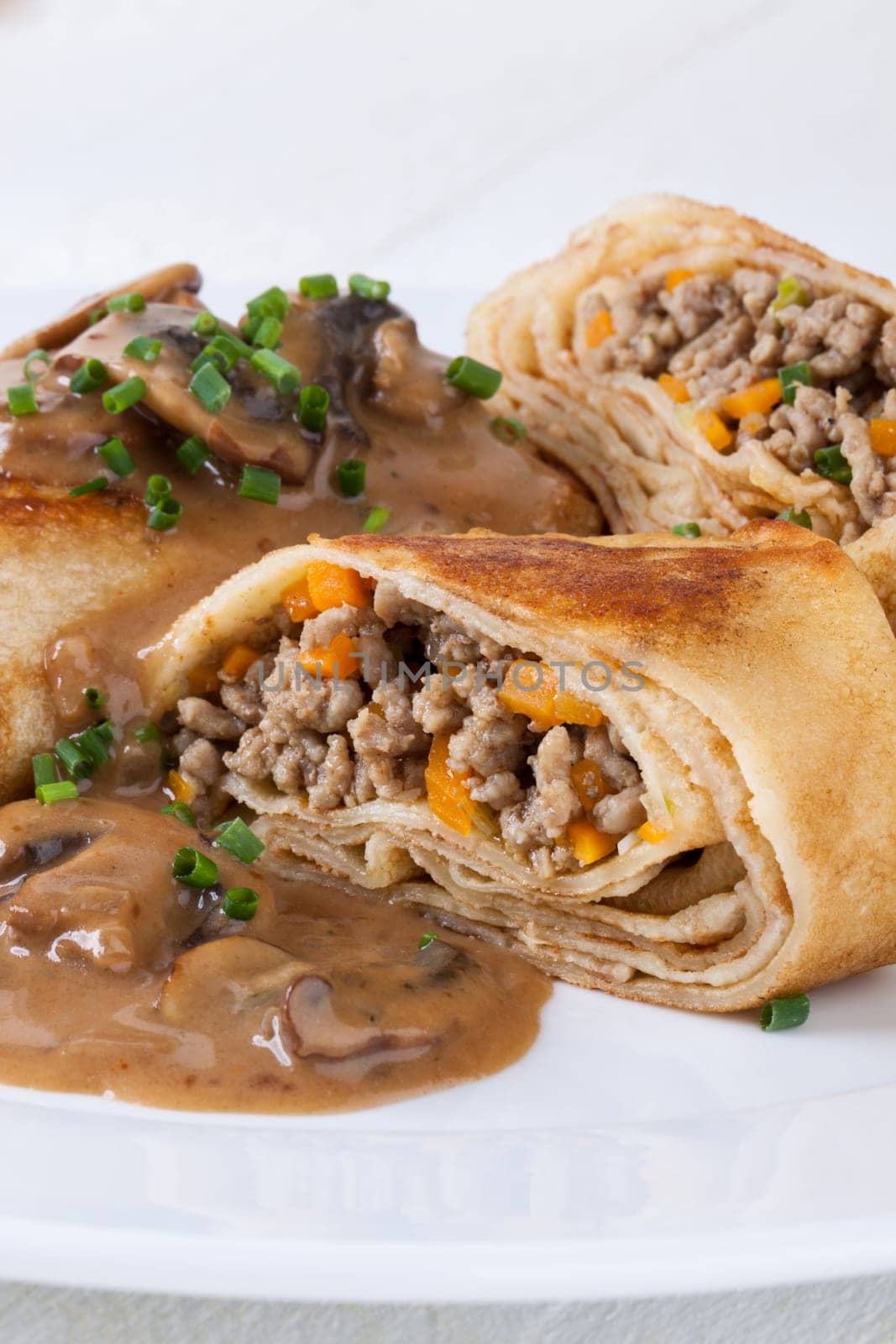 Pancake crepes tortillas stuffed with mushrooms and minced meat on a white plate close-up
