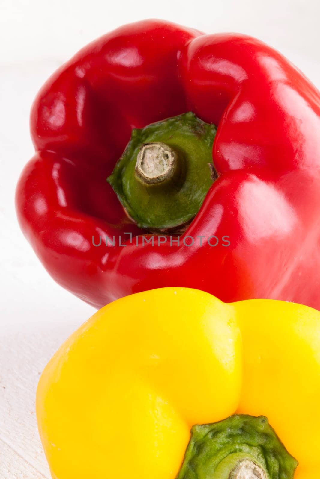 Fresh red and yellow peppers on a white wooden board as a close-up