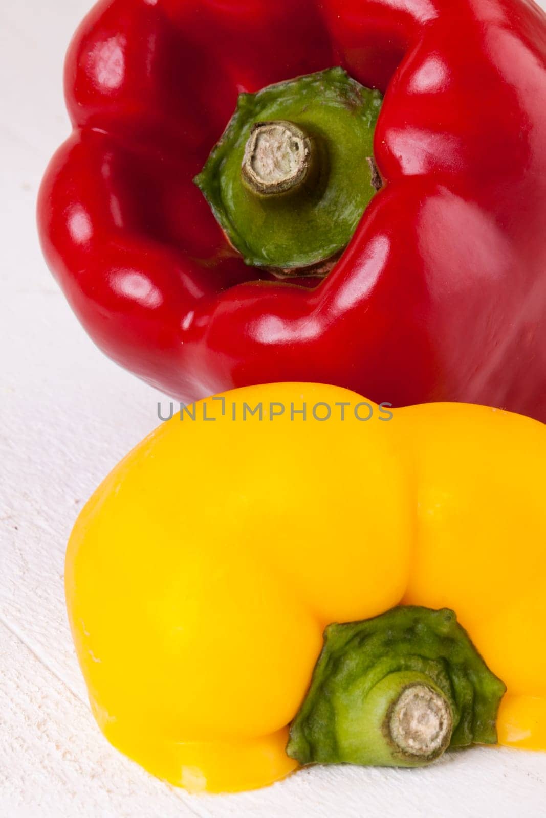 Fresh red and yellow peppers on a white wooden board as a close-up