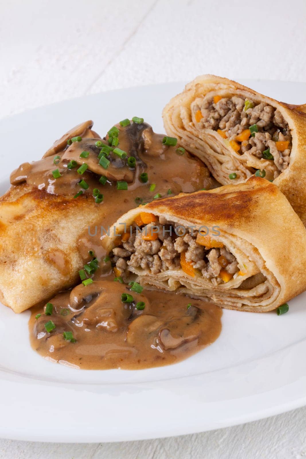 Pancake crepes tortillas stuffed with mushrooms and minced meat on a white plate close-up