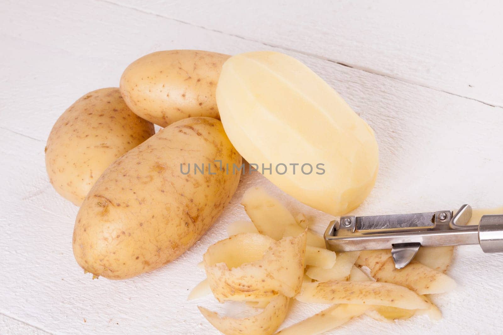 Potatoes with peels and peeled with potato peeler Peeler as close-up