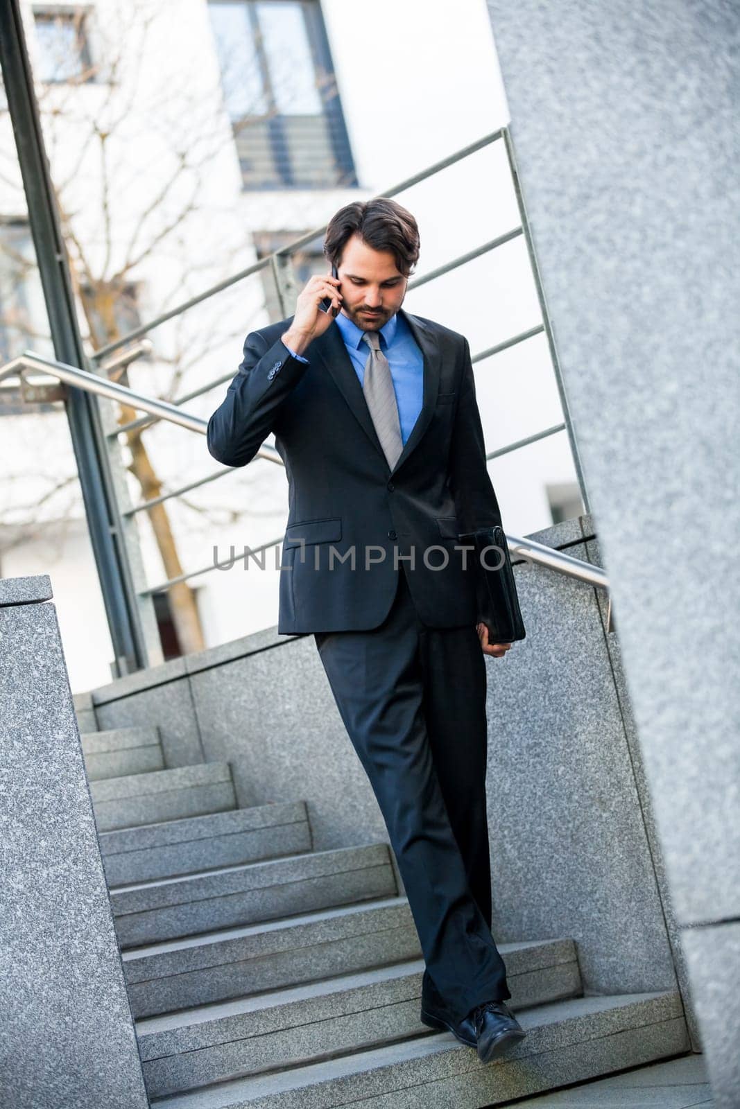 Young trendy successful businessman with mobile phone smartphone cheerful lyrane in front of an outdoor business building