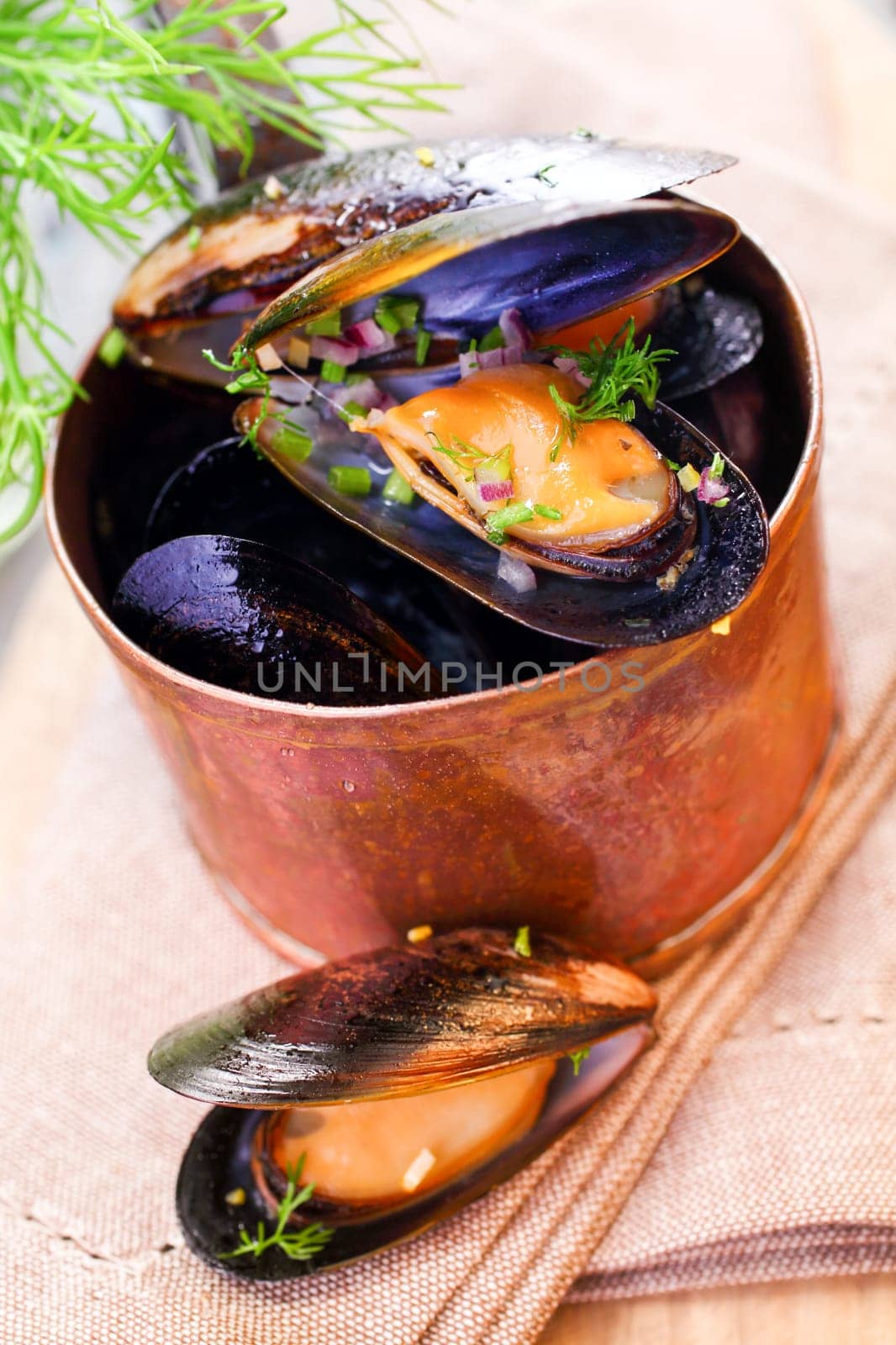Delicious freshly boiled marine mussels in a copper saucepan with their shells open garnished with dill for a gourmet seafood starter, high angle closeup view