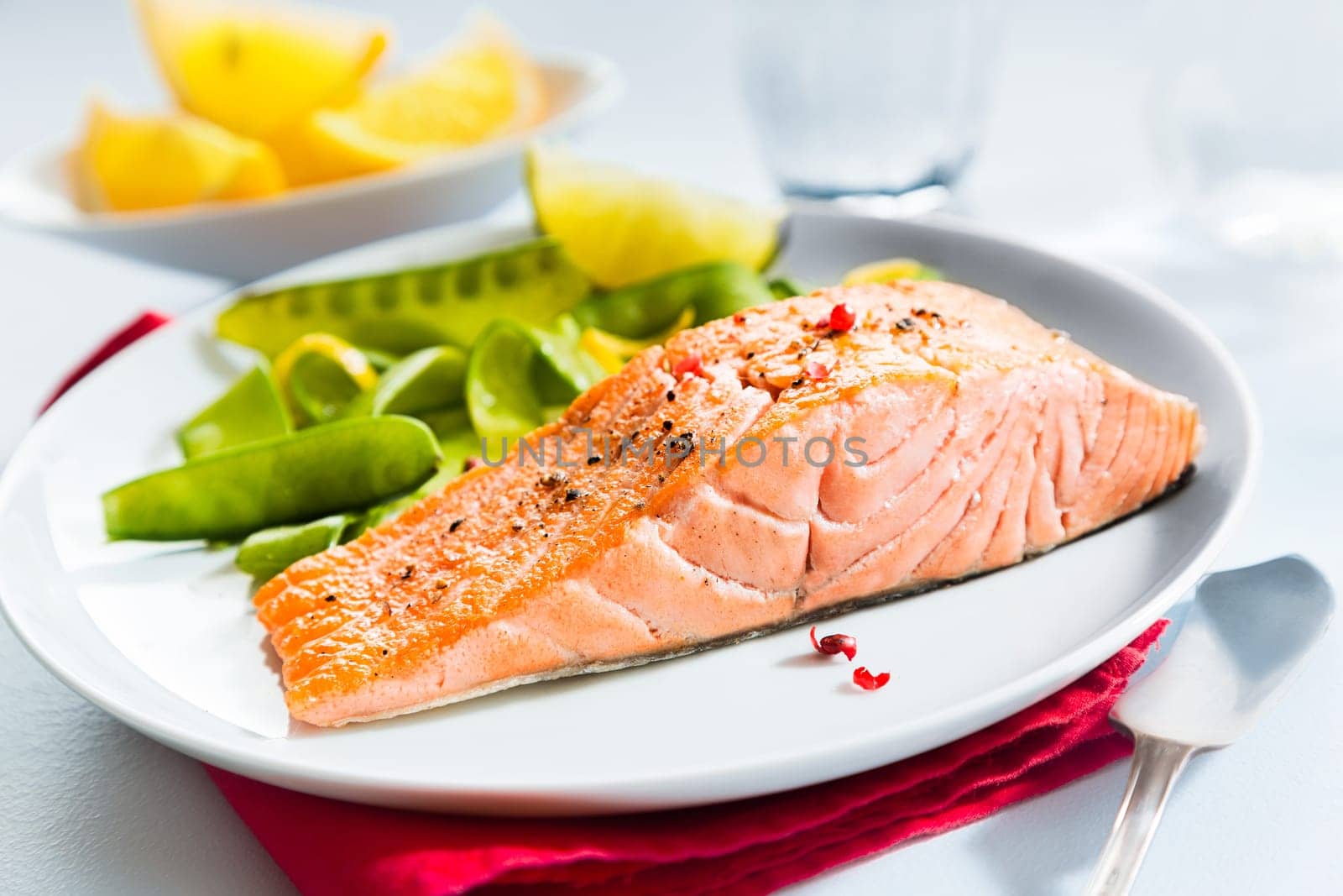 Gourmet seafood meal of grilled salmon steak served with fresh green mangetout peas and lemon wedges for flavoring