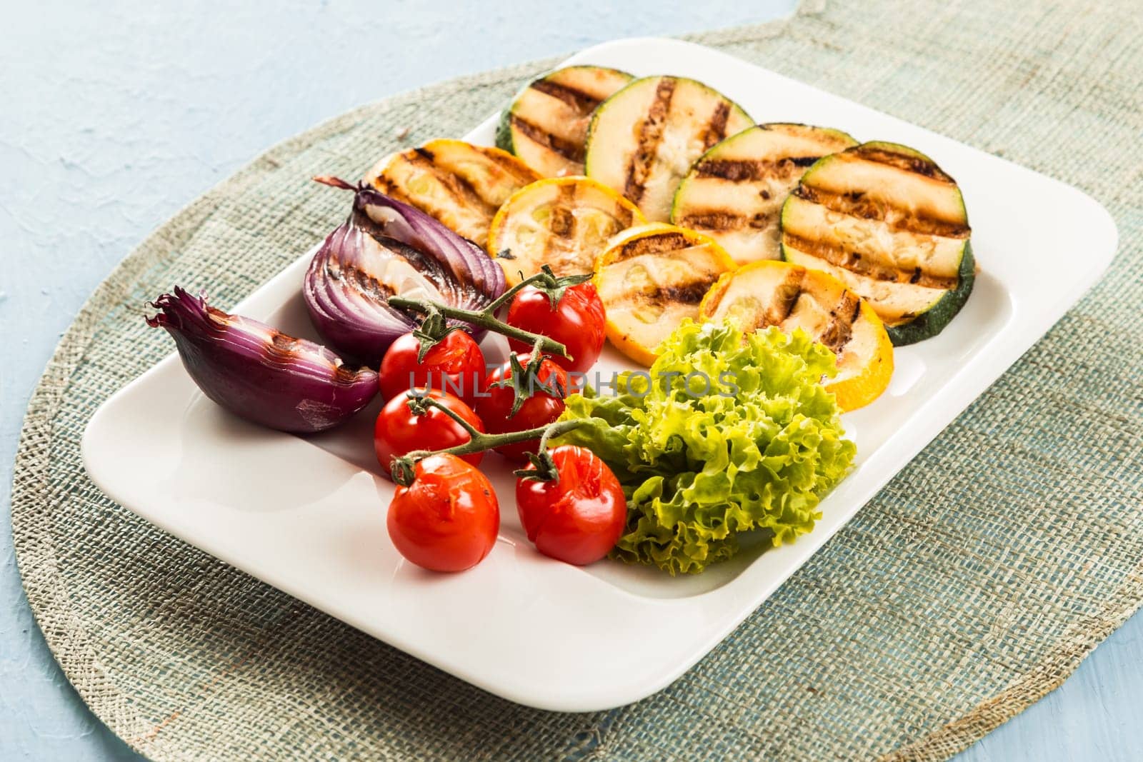 Serving of delicious roasted and fresh vegetables with courgette, zucchini, red onion, cherry tomato and lettuce for a tasty vegetarian snack