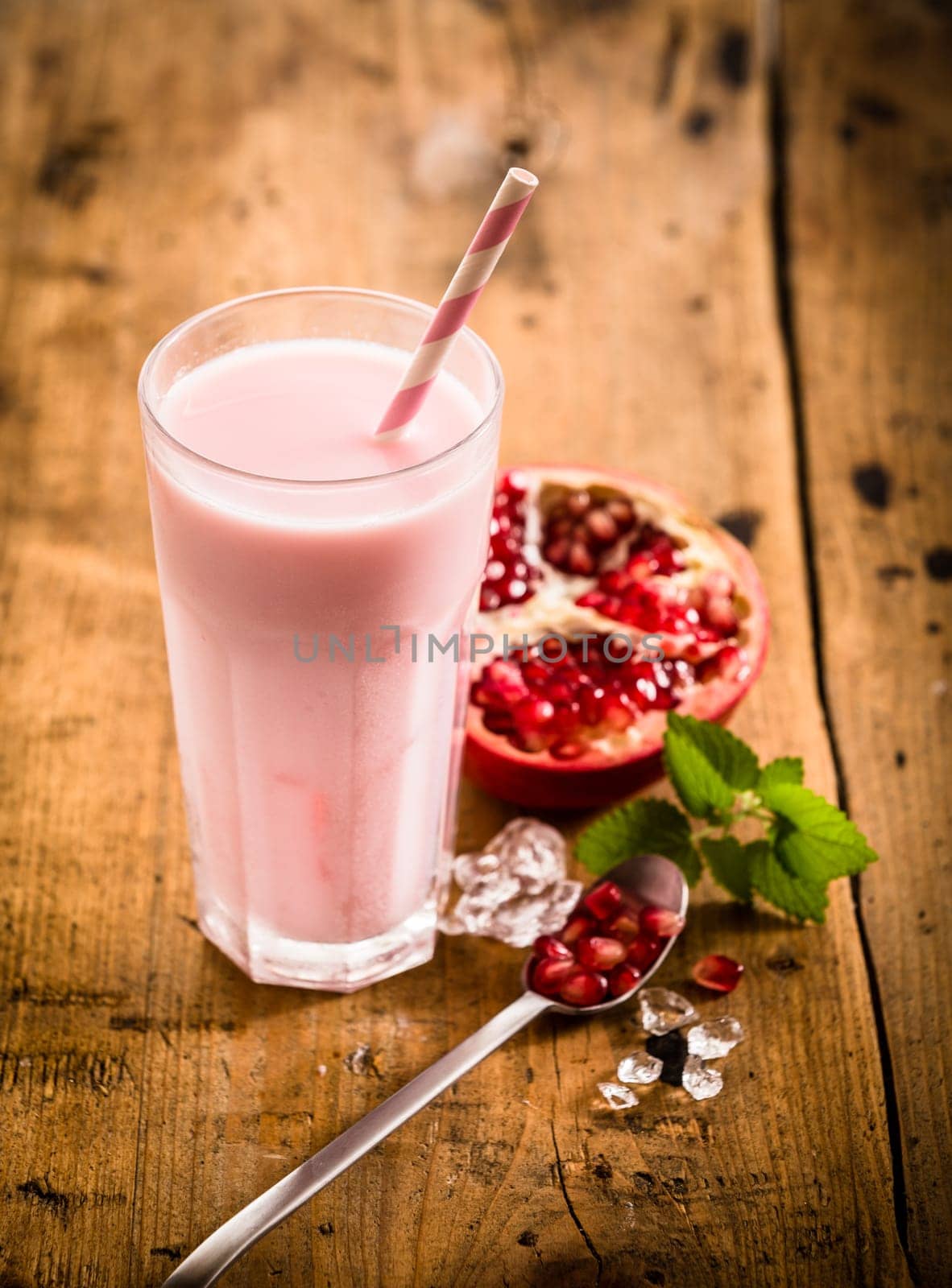 Healthy delicious pomegranate smoothie with a fresh halved pomegranate blended with frozen yoghurt or ice cream on a rustic wooden table, high angle view
