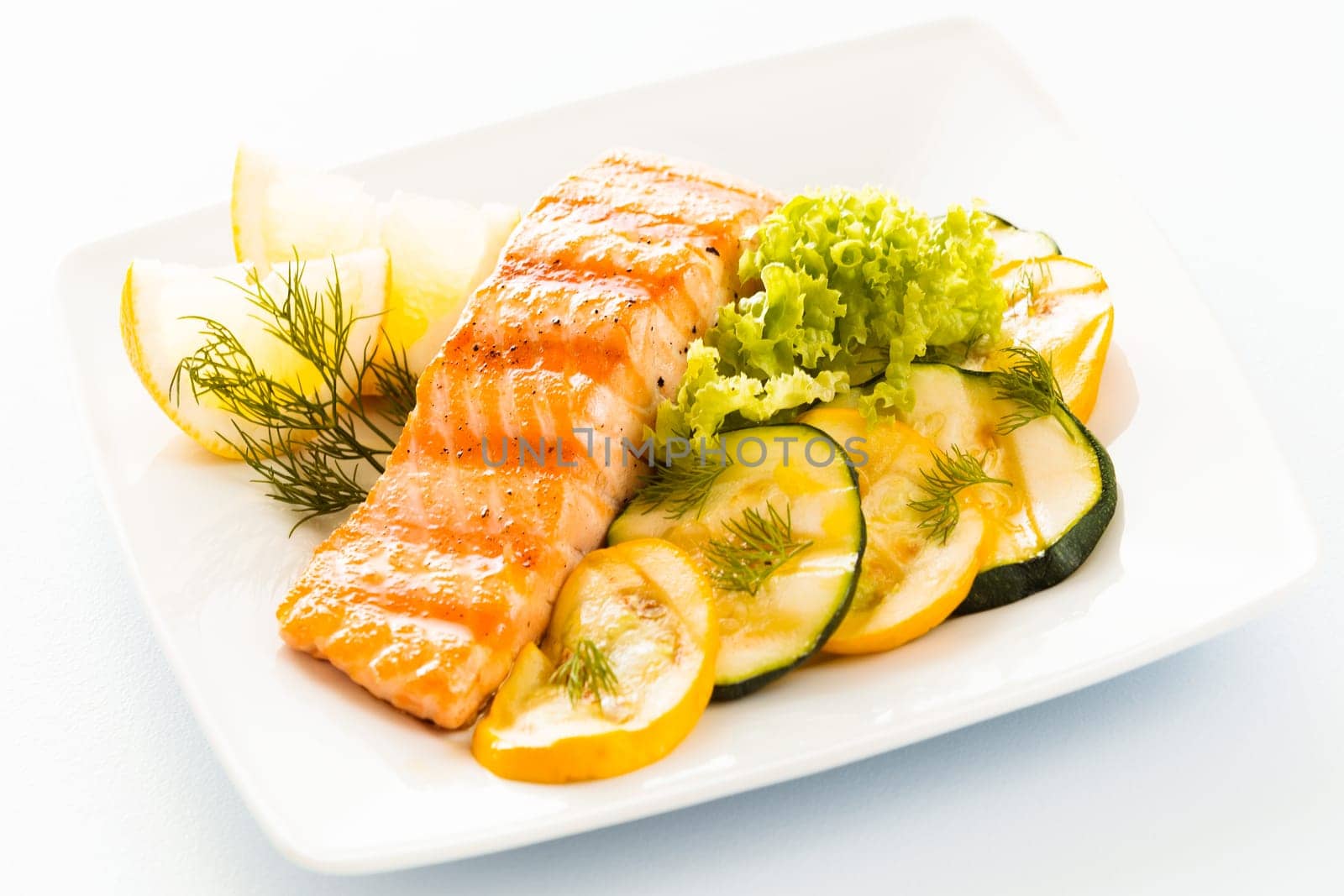 Salmon steak with sliced zucchini and courgette, lettuce and lemon garnished with fresh dill for a tasty seafood platter or appetizer