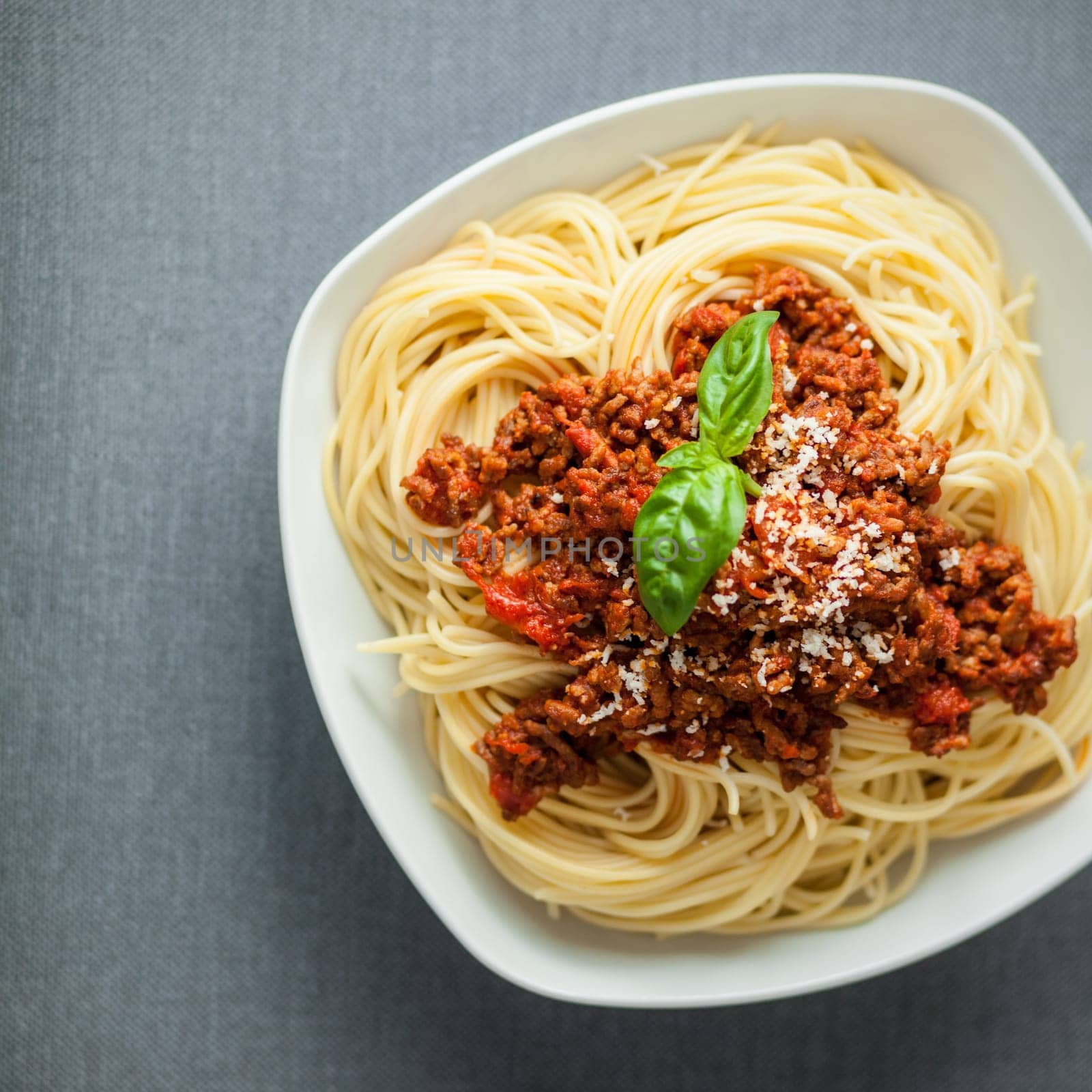 Overhead view of a large bowl of traditional Italian spaghetti pasta with a rich tomato and ground beef Bolognese topping garnished with fresh basil and parmesan cheese