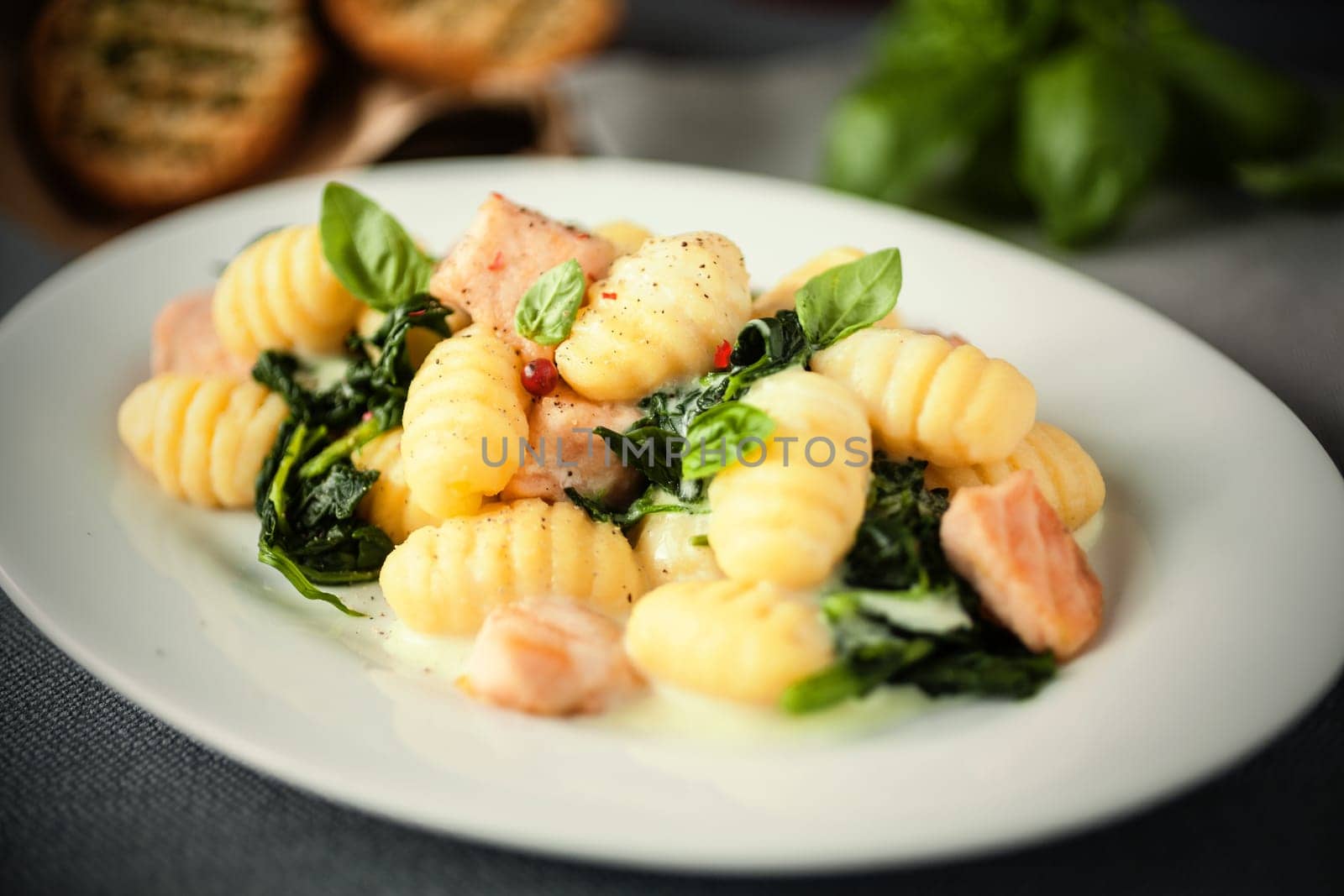 Italian gnocchi pasta, or dumplings, with grilled salmon pieces and fresh basil on an oval plate