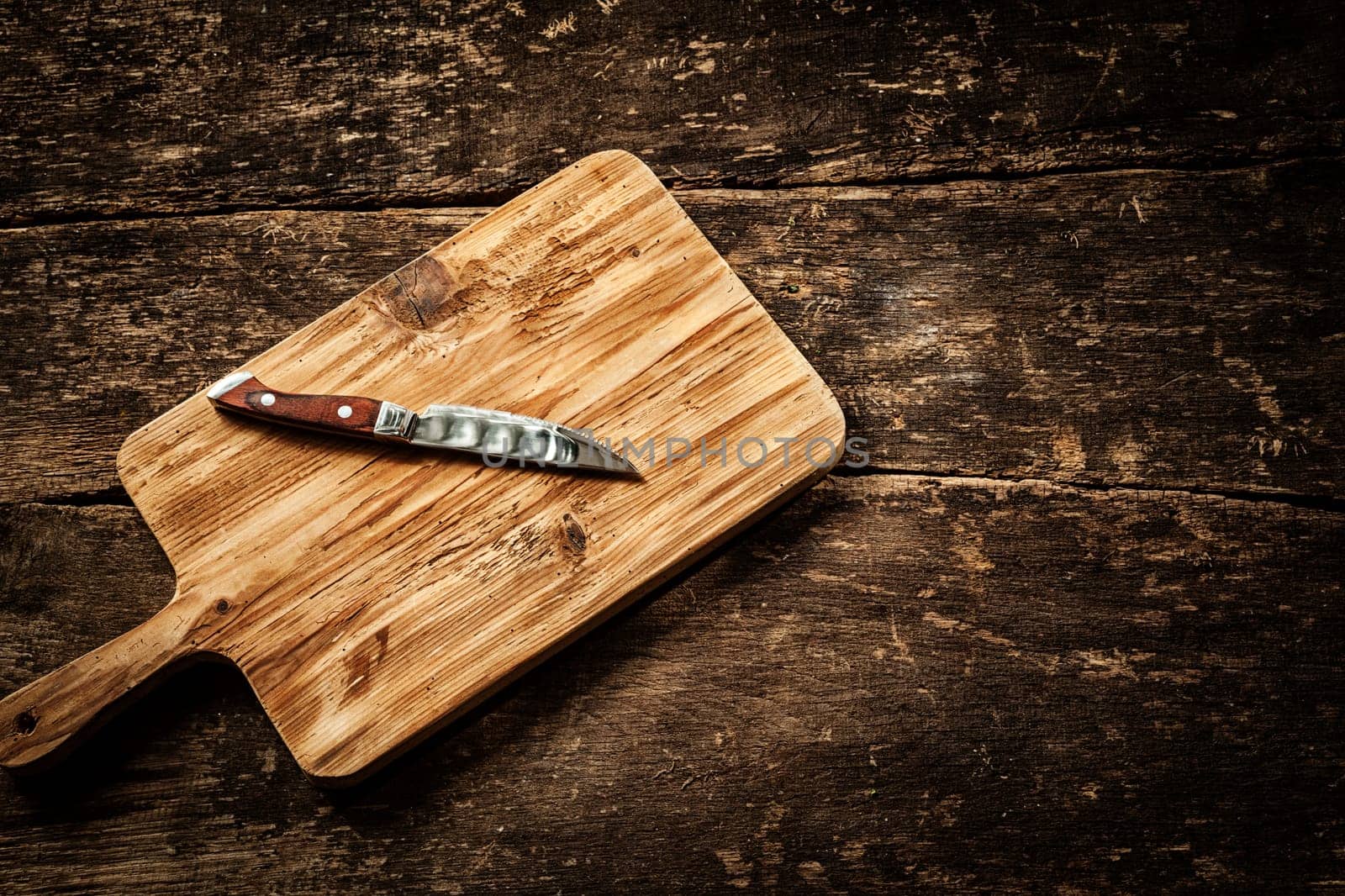 Empty chopping board with a sharp paring knife on a distressed grunge wooden table in a rustic kitchen, overhead view with a vignette and copyspace