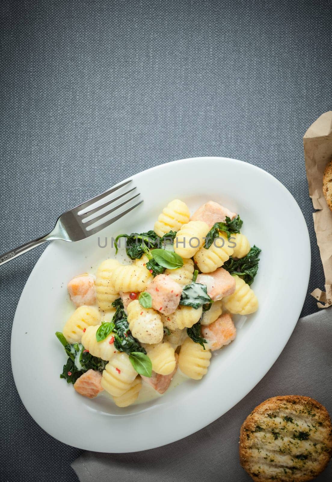 Traditional Italian cuisine with a plate of gnocchi pasta, or dumplings, made with semolina and served with basil and grilled salmon cubes, view from above on grey with copyspace