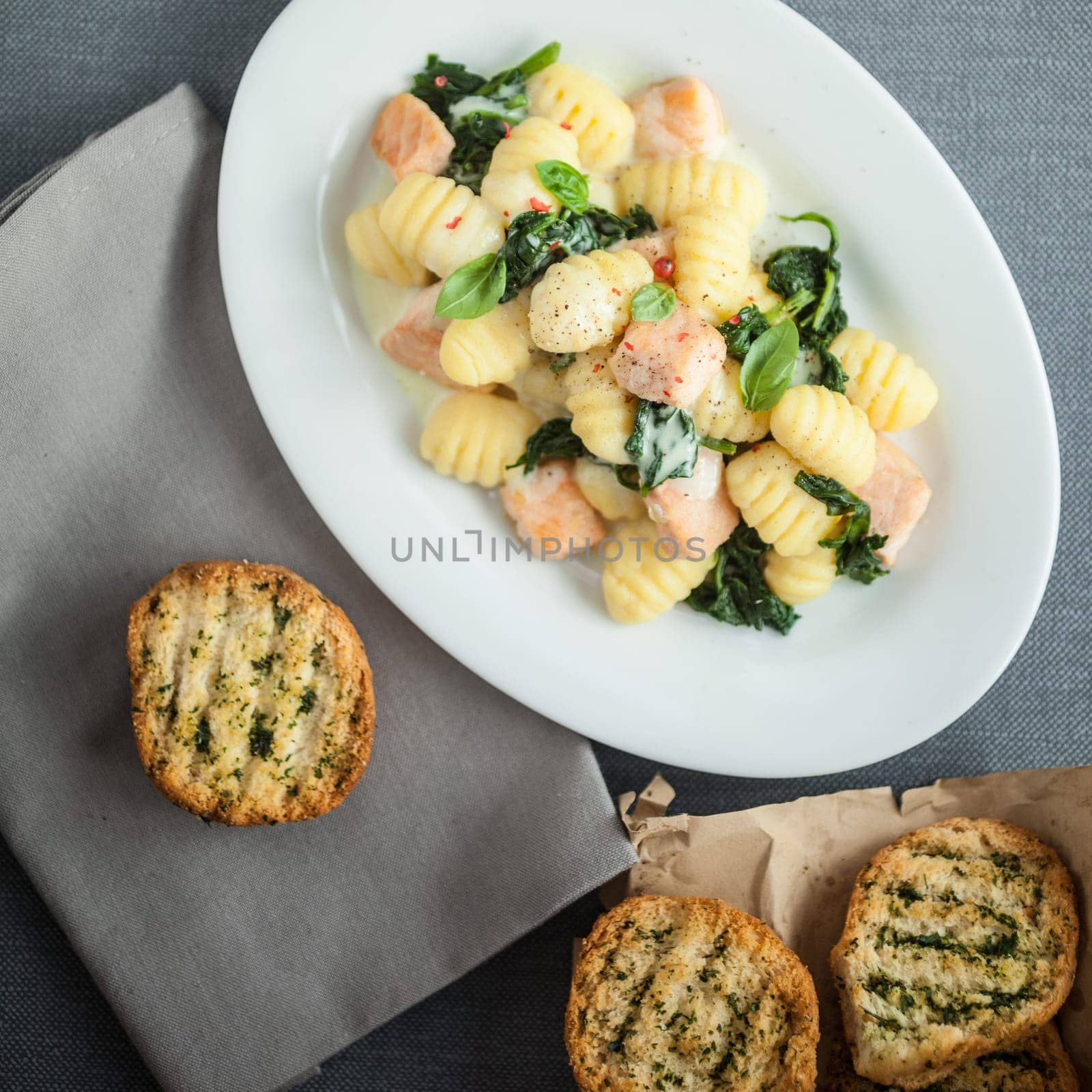 View from above of a plate of Italian gnocchi pasta , basil and grilled salmon pieces served with crisp crusty toasted herbal buns