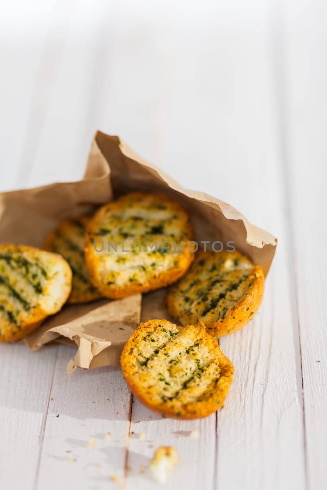 Golden crunchy grilled herb bread from the BBQ spilling from a torn brown paper packet on a rustic white wooden picnic table with copyspace