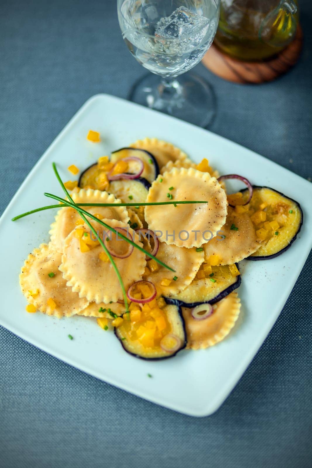Delicious Italian vegetarian cuisine with round girasole ravioli and aubergine or eggplant topped with chives and served with a glass of wine