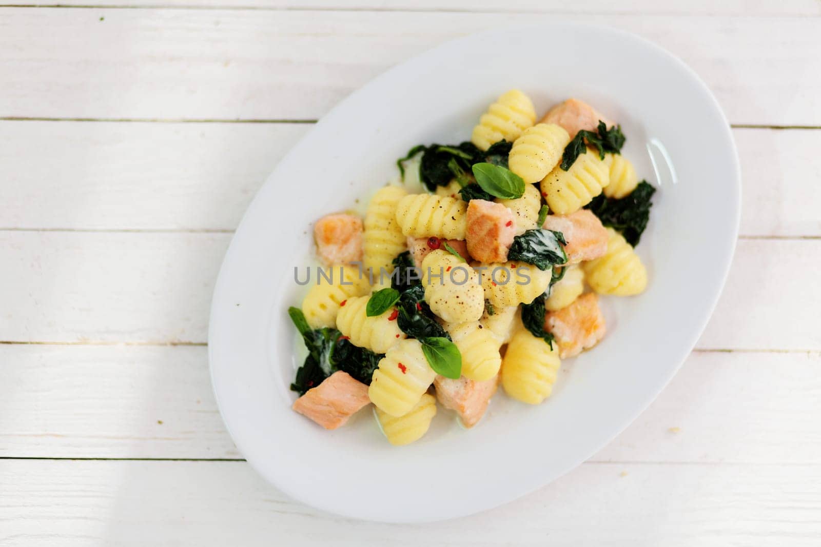 Overhead view of a plate of sauteed Italian gnocchi with salmon and basil on a rustic wooden white picnic table for a healthy lunchtime snack, with copyspace