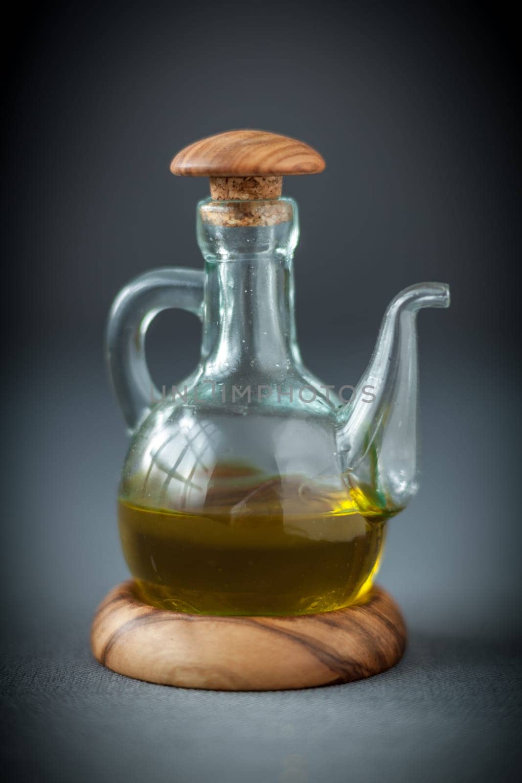 Transparent glass decanter with a wooden stopper half filled with healthy olive oil to use as a dressing for salads or cooking ingredient, on grey