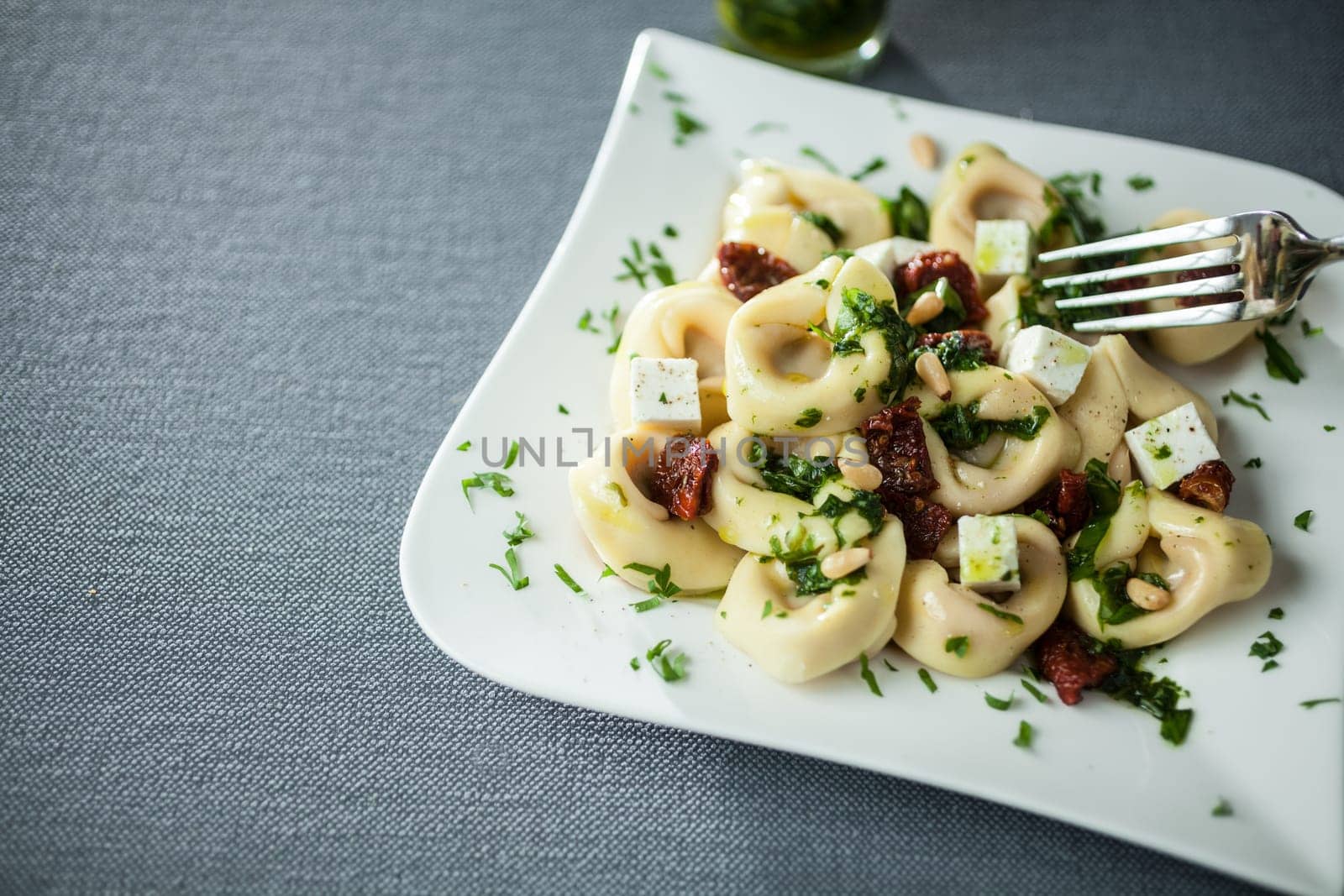 Serving of feta cheese, basil and pine nut pesto with Italian tortellini pasta on a modern curved white plate over a grey cloth with copyspace