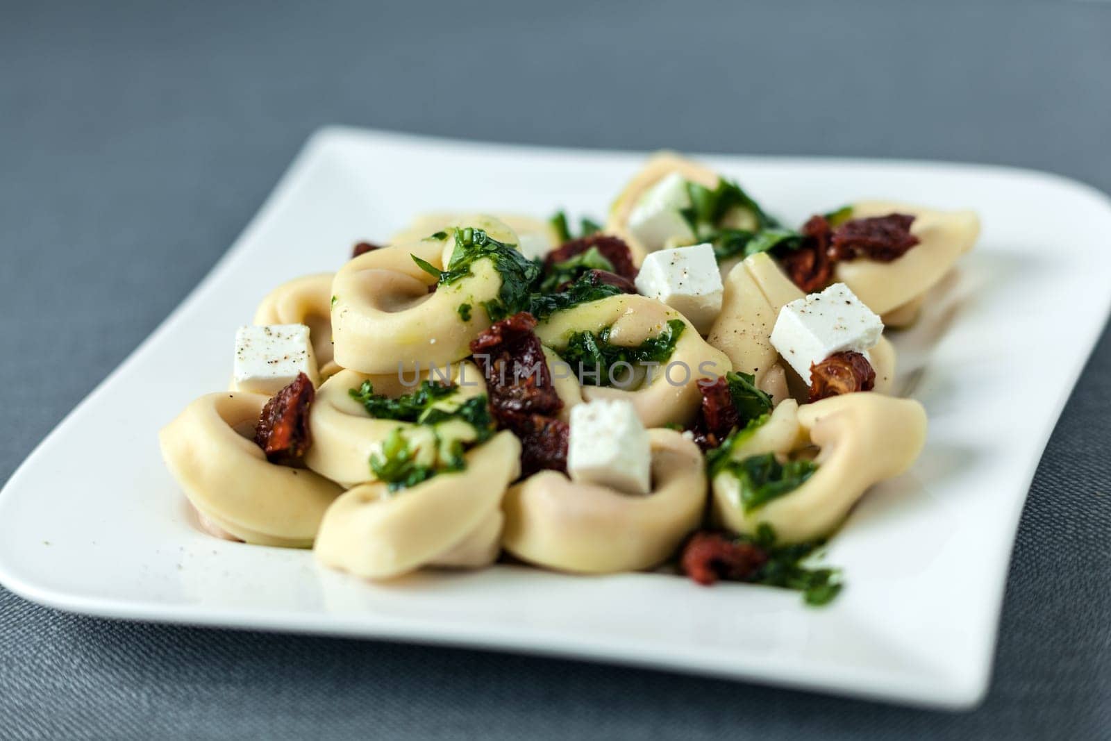 Stuffed tortellini Italian pasta with feta cheese, pine nuts and pesto sauce on a modern curved plate