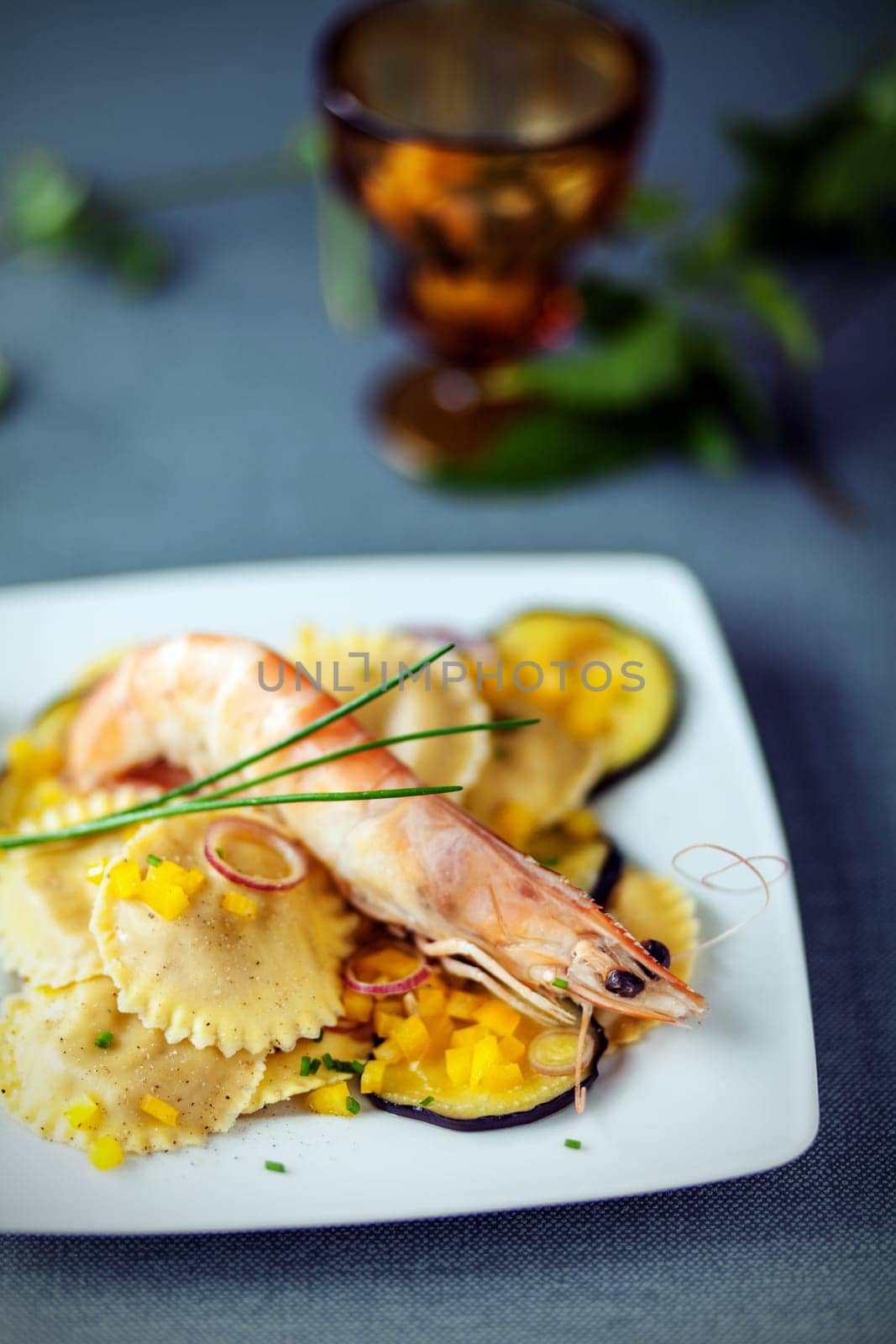 Seafood starter with prawns, Italian ravioli pasta and roasted slices of aubergine or eggplant garnished with fresh chives