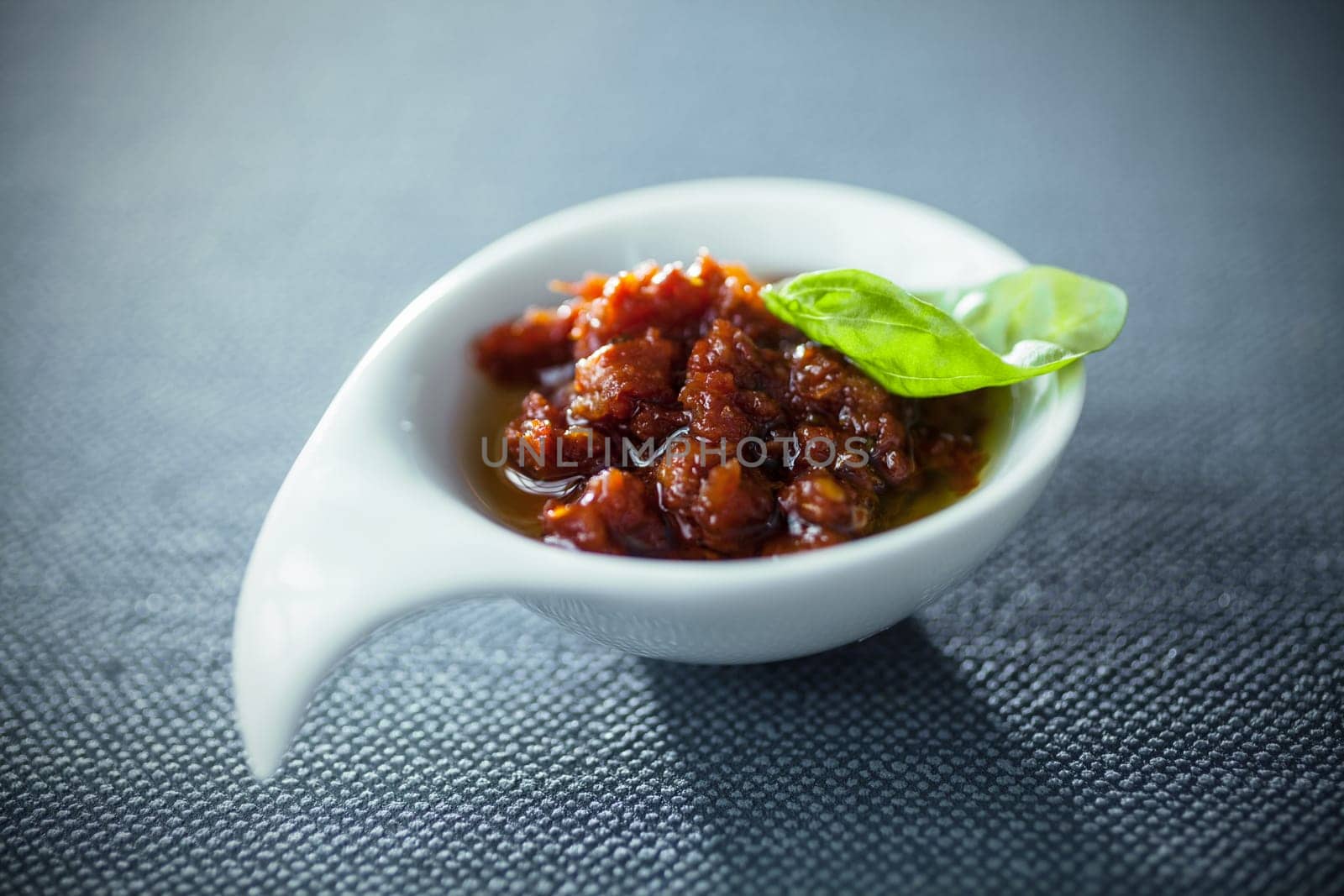 Spicy savory dip or chutney with tomatoes and chili in a modern stylish bowl garnished with fresh basil