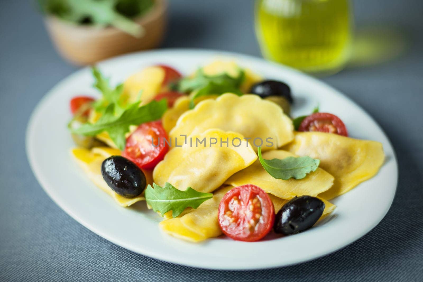 Italian ravioli salad with rocket , cured black olives and fresh cherry tomato on an oval plate, closeup with shallow dof