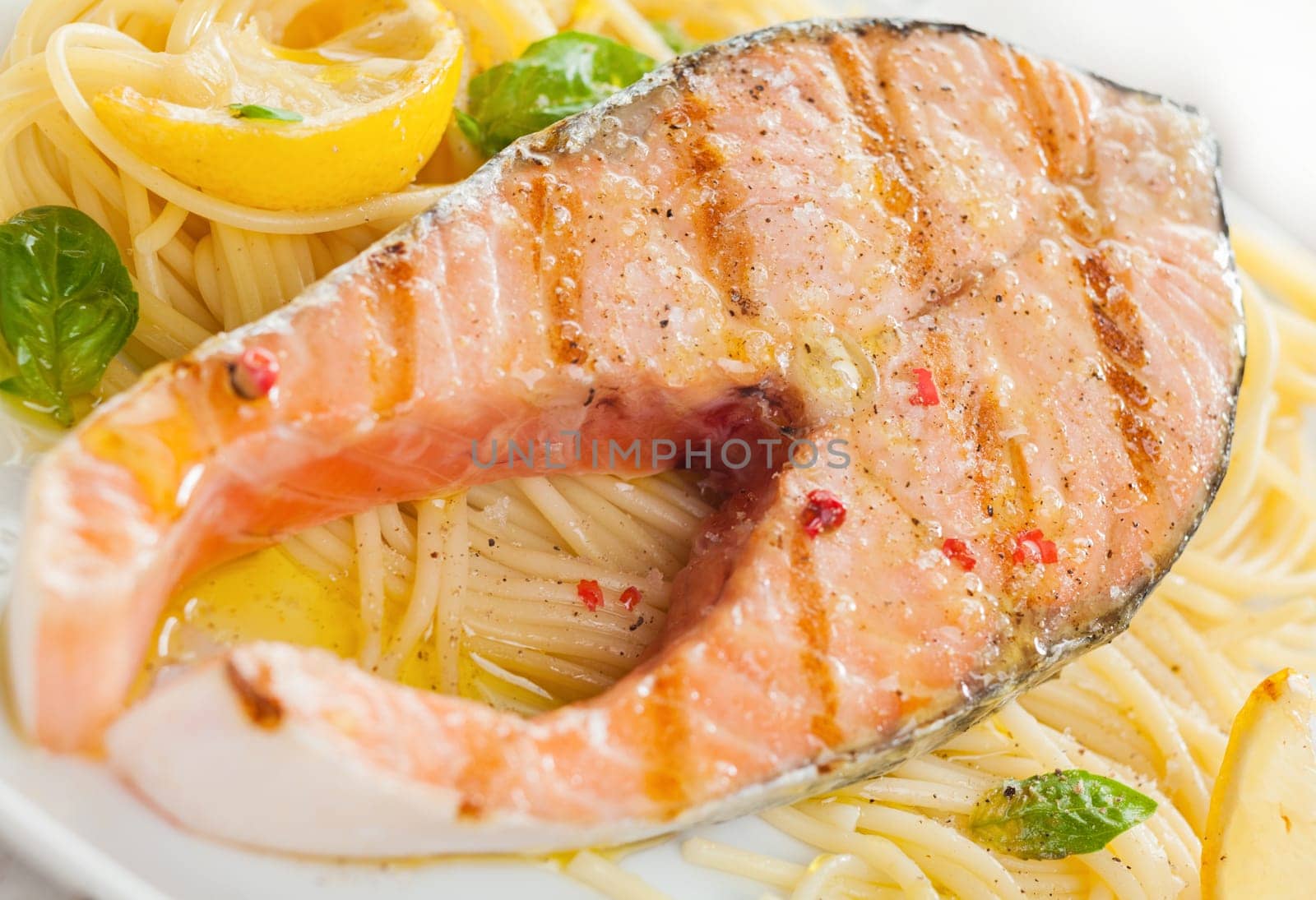 Grilled salmon cutlet with linguine pasta, basil and lemon for a gourmet Italian seafood dinner, close up view and texture