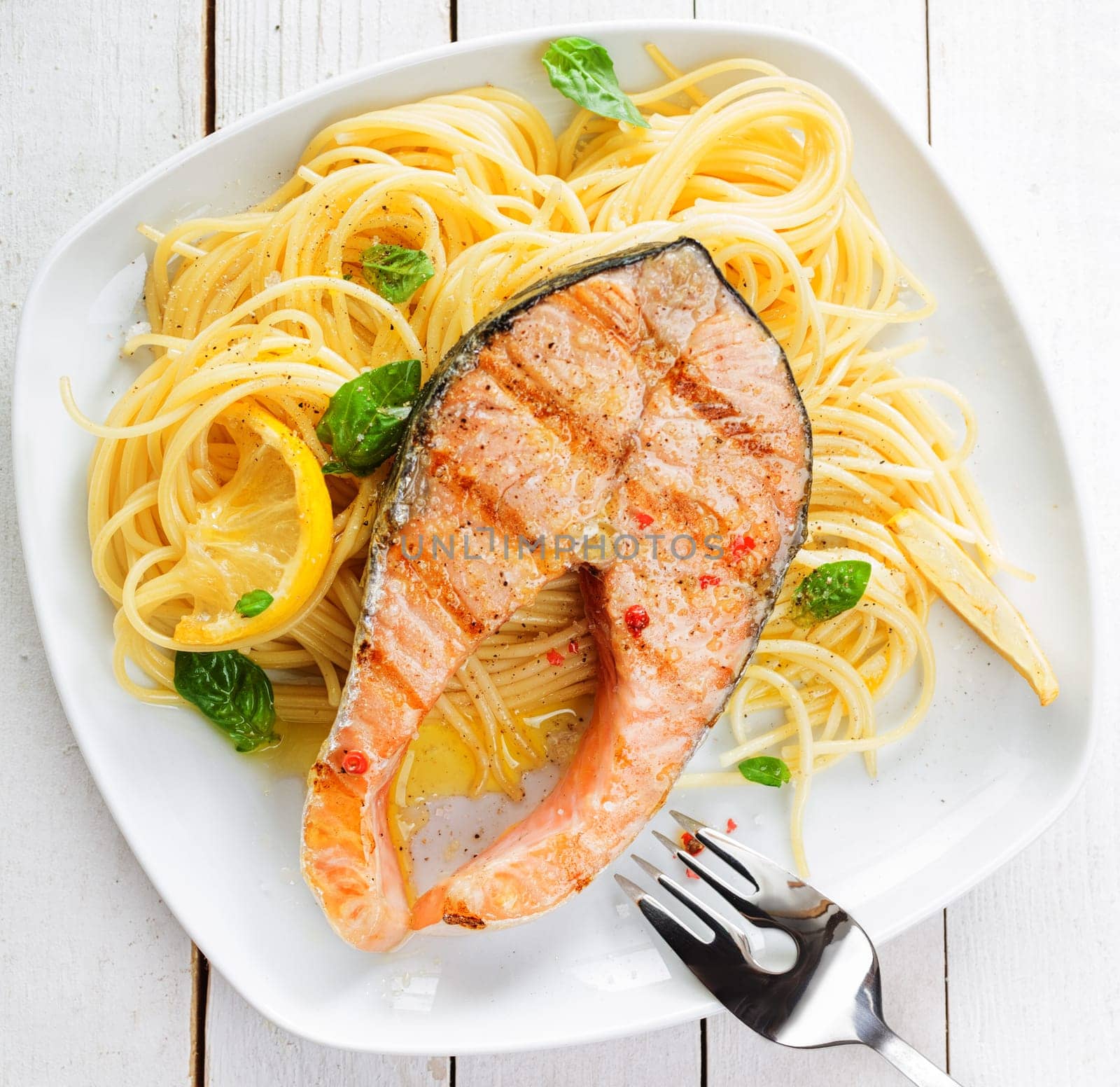 Healthy grilled salmon steak rich in omega-3 fatty acids served on linguine pasta topped with fresh basil , overhead view