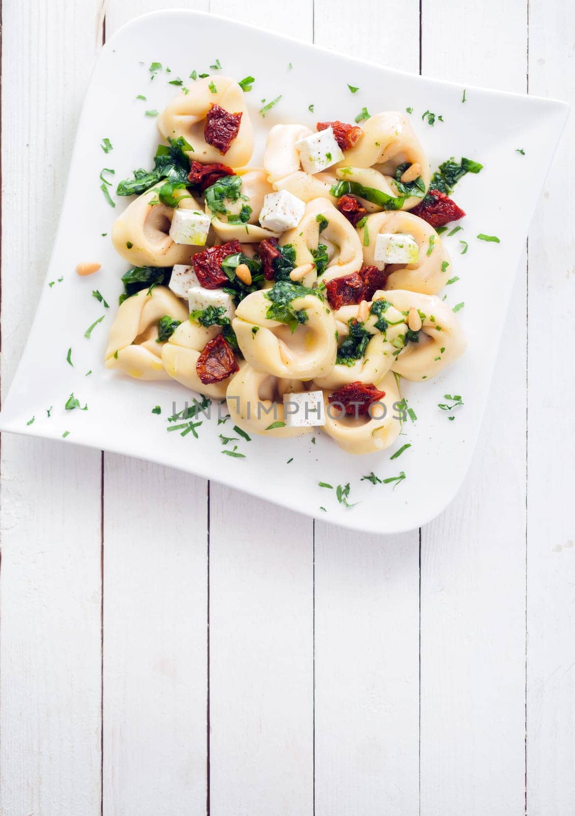 Tortellini pasta with fresh herbs, a spicy piquant sauce and feta cheese on an elegant plate on a white wooden table with copyspace