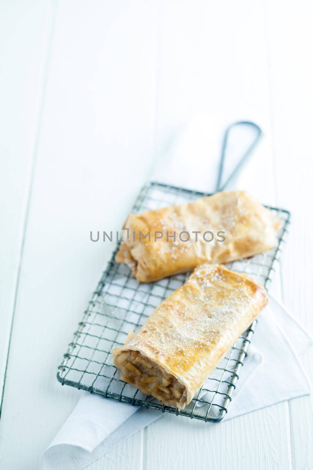 Fresh German apfelstrudel or apple strudel with delicious light puff pastry enclosing an apple filling dusted with powdered sugar served on a wire rack in a country restaurant, high key with copyspace