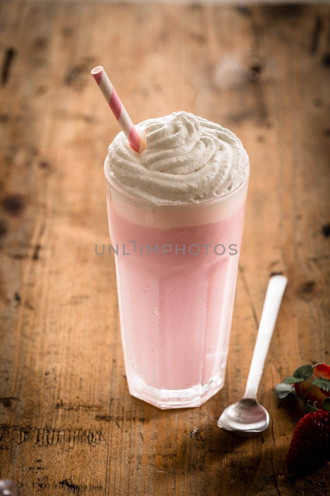 Delicious berry smoothie or milkshake served in a tall glass topped with a twirl of whipped cream or frozen yoghurt, high angle view on a rustic wooden counter