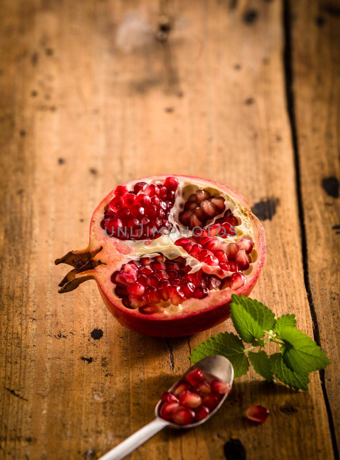 Halved fresh pomegranate with seeds in a teaspoon rich in vitamins and used in ayurvedic medicine on a rustic wooden table with copyspace