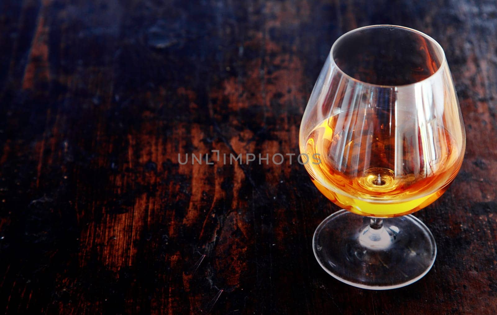 Glowing cognac or brandy in an elegant snifter glass on an old dark wooden bar counter with copyspace, high angle view